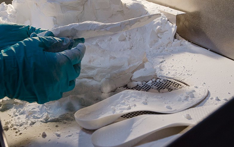 Pulling finished orthotic from SLS 3D printer powder bed